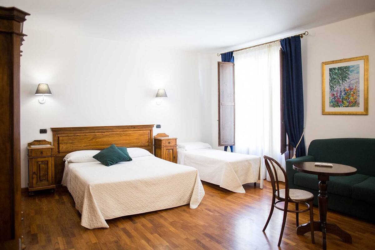 Ein Hotelzimmer mit zwei Betten, Holzboden, einem grünen Sessel, einem kleinen Tisch und einem Bild an der Wand.