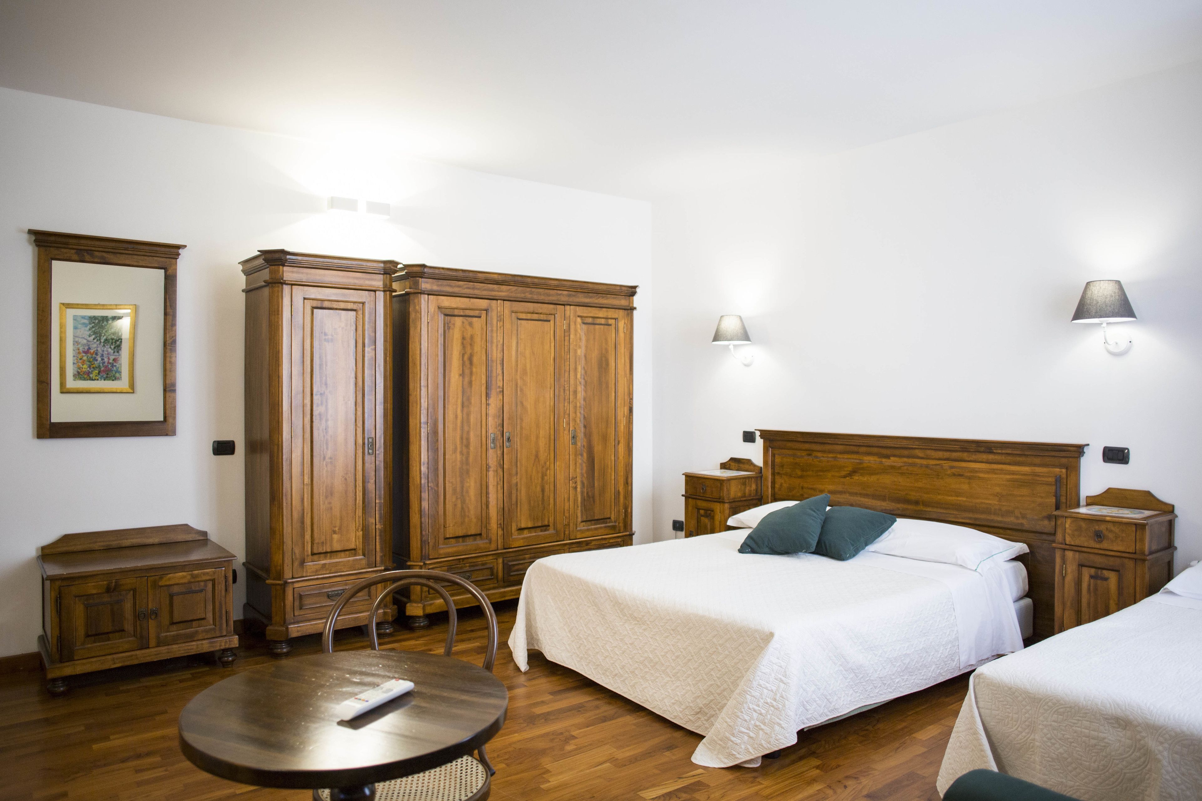 Una habitación de hotel con un armario de madera, una cama con ropa de cama blanca, una mesa redonda y dos mesitas de noche.