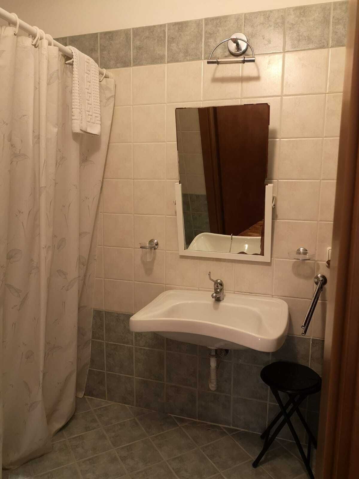 A bathroom with a shower curtain, a sink, a mirror, and a small stool.