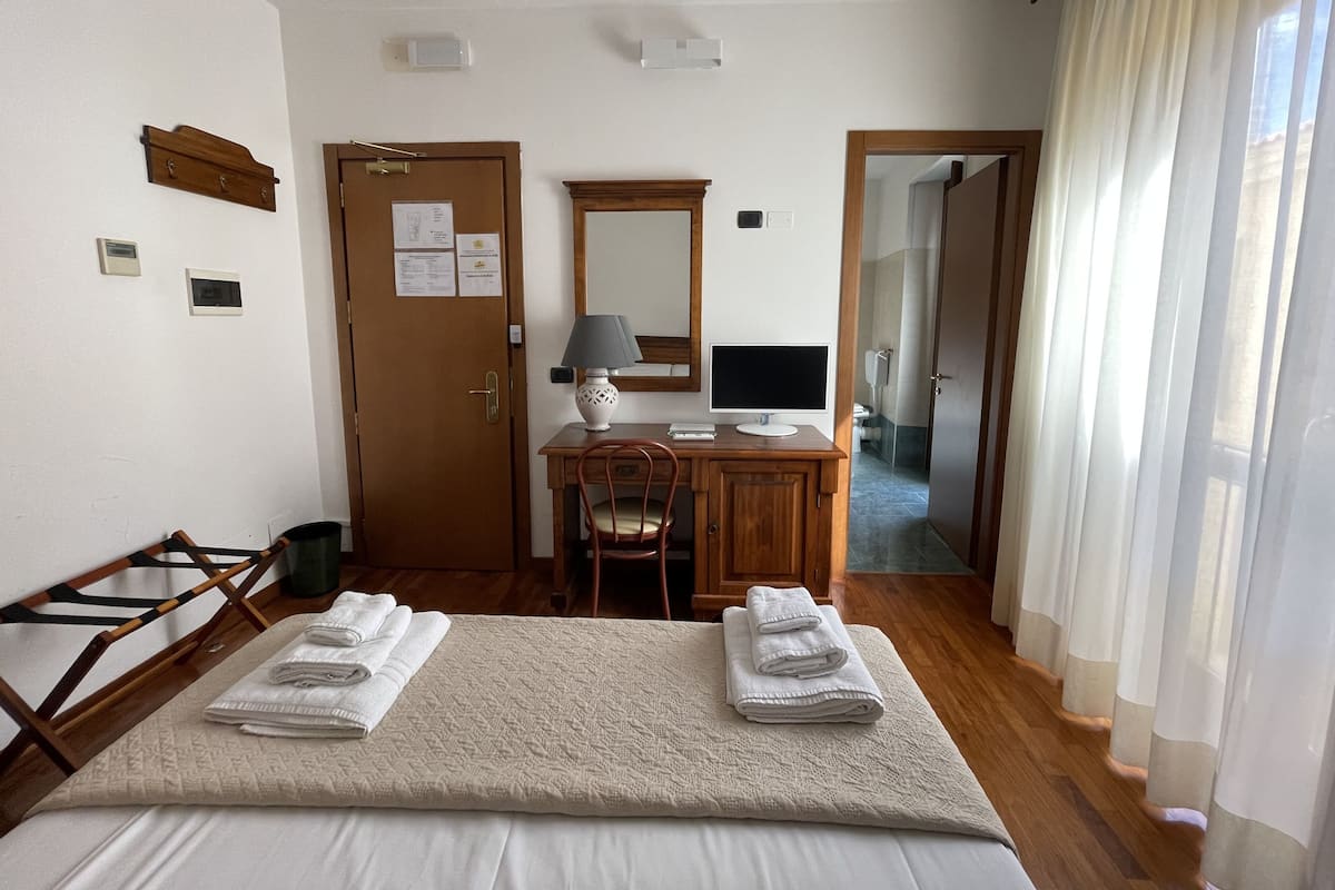 Ein Hotelzimmer mit einem Bett, einem Schreibtisch mit Computer, einem Stuhl und einer Tür.