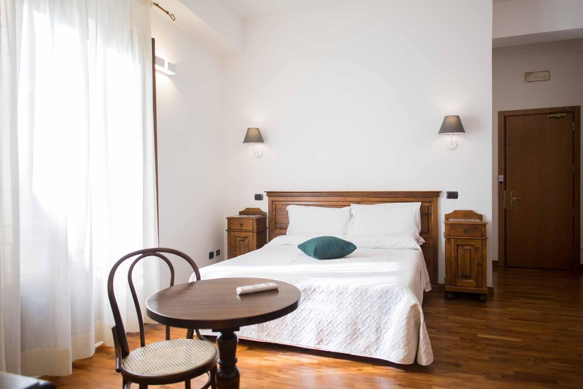 A hotel room with a wooden bed, a round table with a chair, and a wooden wardrobe.