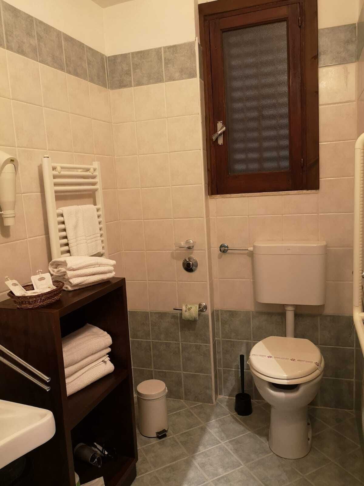 A bathroom with a toilet, a sink, a towel rack, a trash bin, and a shower area.