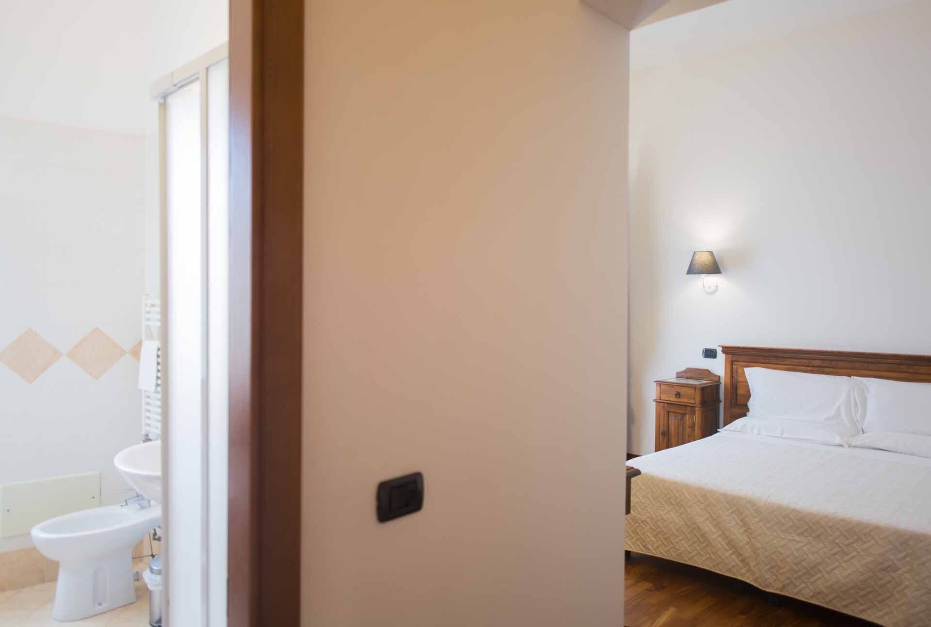 A hotel room with a bed, a bedside table, a lamp, and a toilet visible through an open door.