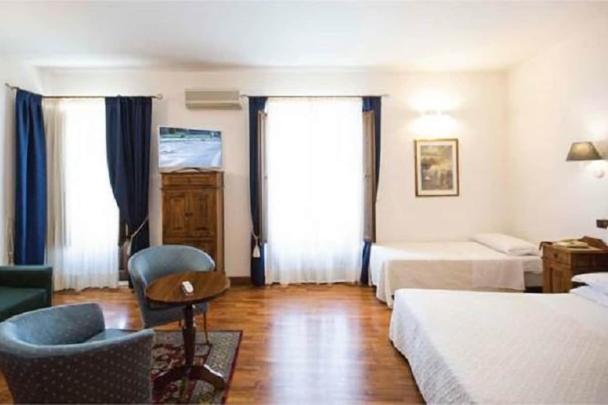 Une chambre d’hôtel avec un lit, une chaise, un canapé, une armoire en bois et un tableau au mur.