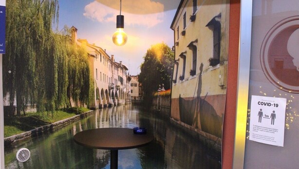 Un comedor con un mural de un canal, dos taburetes y una mesa.