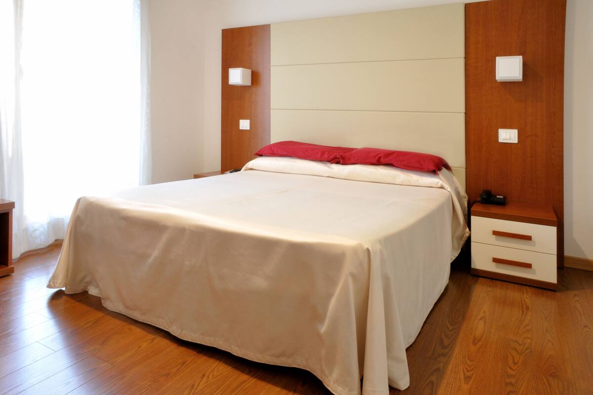 A neatly made bed with a white and red bedspread, a wooden headboard, and a bedside table with a lamp.
