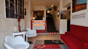 Vestíbulo de hotel con una escalera, una recepción y un sofá rojo.