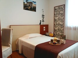 Habitación de hotel con cama, sillón, bandeja con tazas y pared con cartel y cuadro.