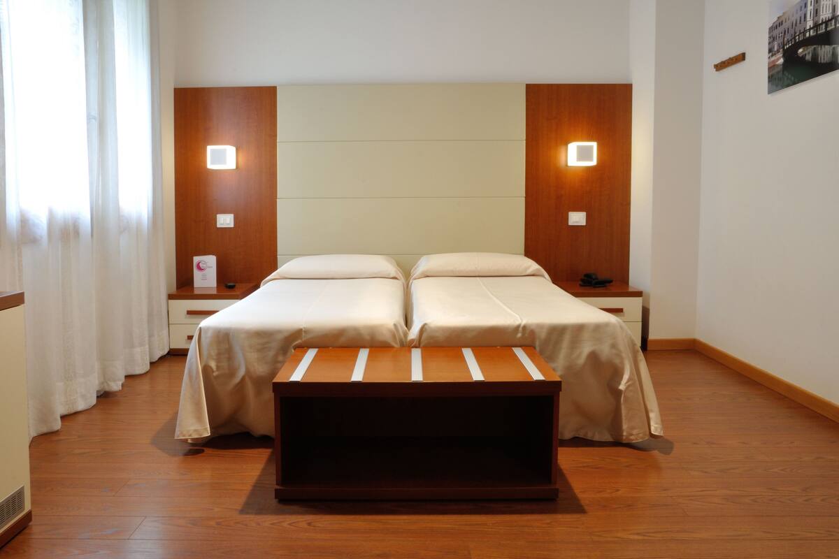 A hotel room with two beds, wooden headboards, bedside tables, and a bench.