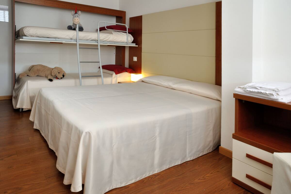 A hotel room with two beds, a wooden floor, and a small desk with a lamp.