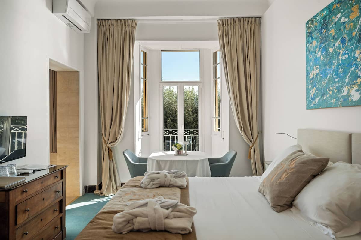 Ein Hotelzimmer mit Bett, Schreibtisch mit Computer, Fernseher, Fenster mit Vorhängen und einem Bild an der Wand.