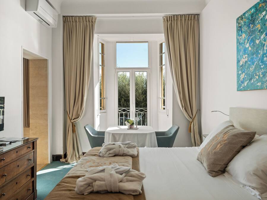 Habitación de hotel con una cama, un escritorio con computadora, televisor, ventana con cortinas y un cuadro en la pared.
