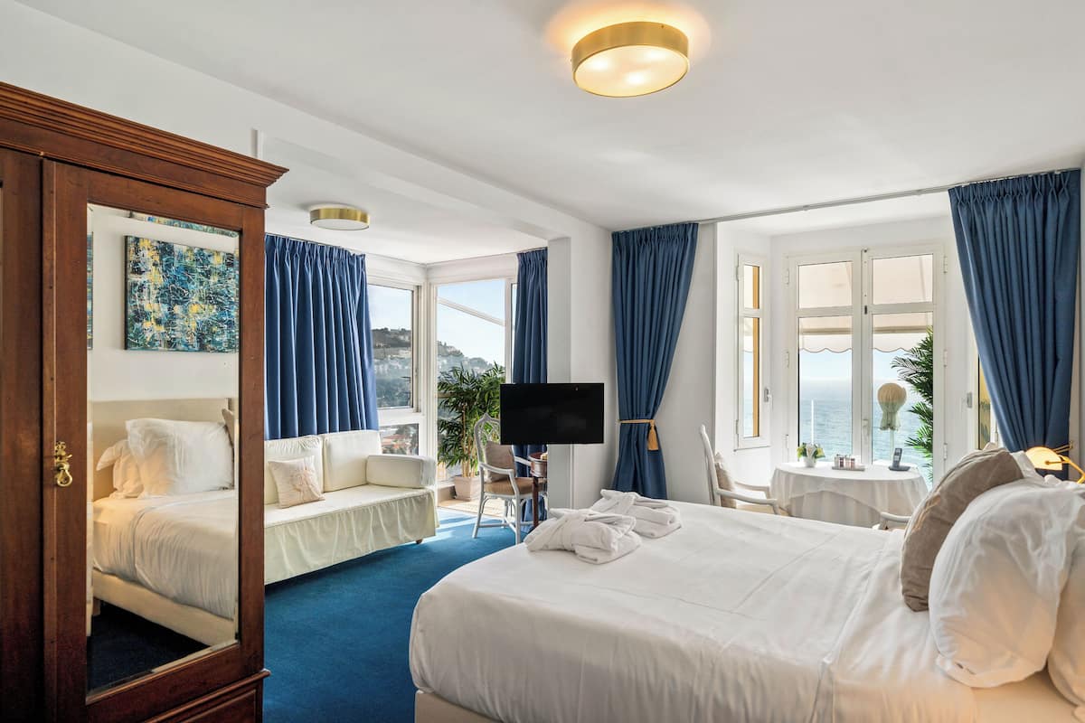 Ein Hotelzimmer mit einem großen Bett, einem Schreibtisch, einem Sessel, einem Fernseher und Blick auf das Meer.