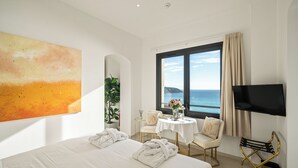 A hotel room with a large bed, a TV, a window with a view of the sea, and a painting on the wall. - Le Roquebrune (Roquebrune-Cap-Martin)