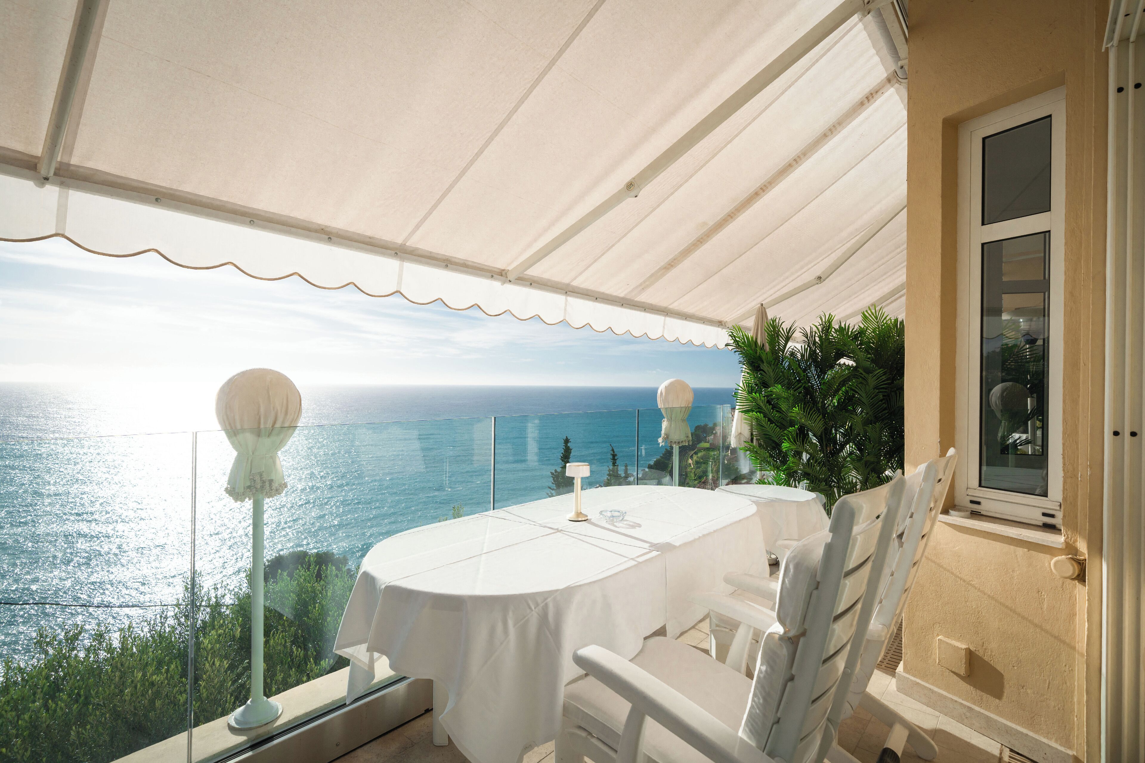 A covered outdoor dining area with a table and chairs, overlooking a coastal view.