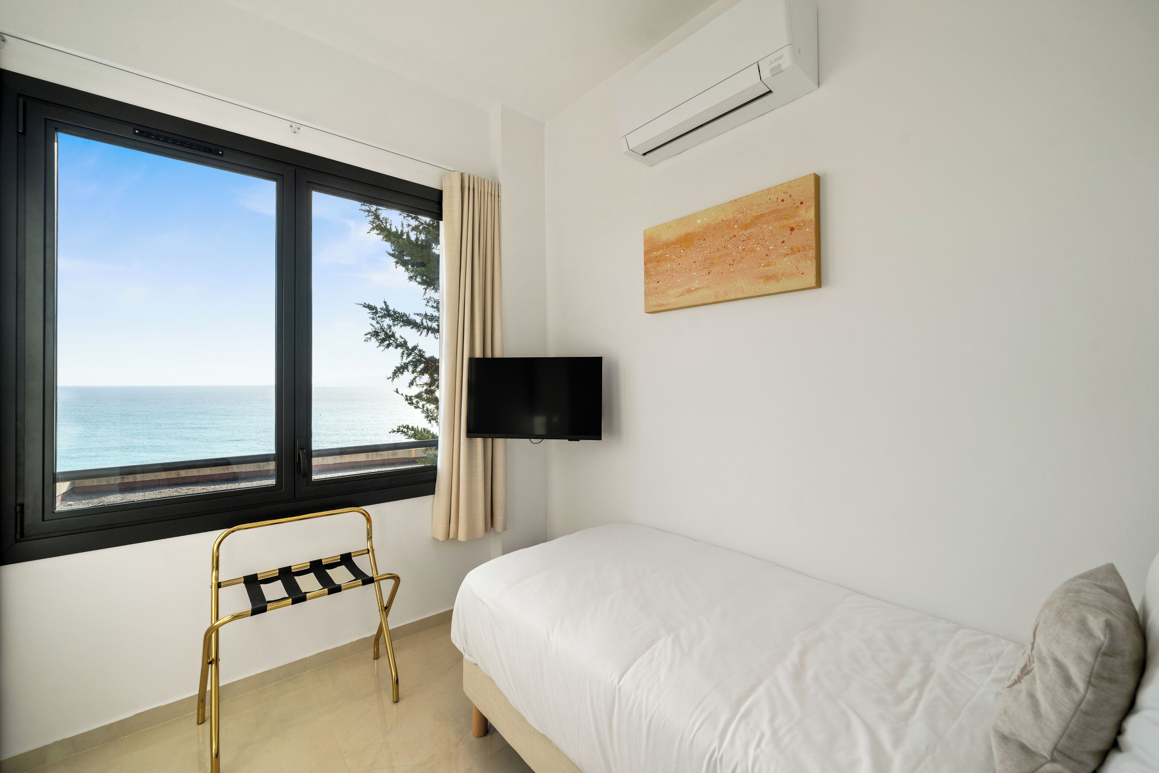 Une chambre à coucher avec un lit, une télévision, un tableau et une fenêtre donnant sur la mer.
