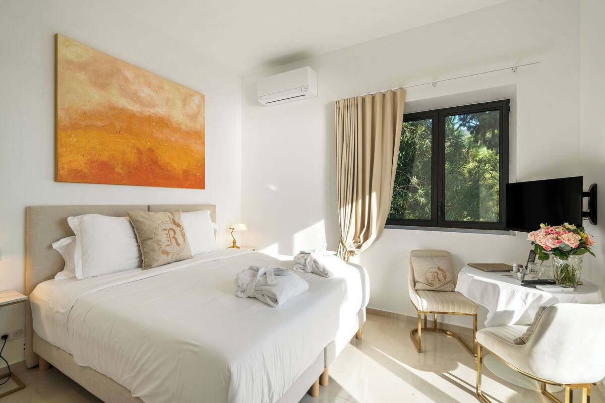 Ein Hotelzimmer mit einem großen Bett, einem Schreibtisch mit Stuhl, einem Fenster mit Vorhängen und einem Bild an der Wand.