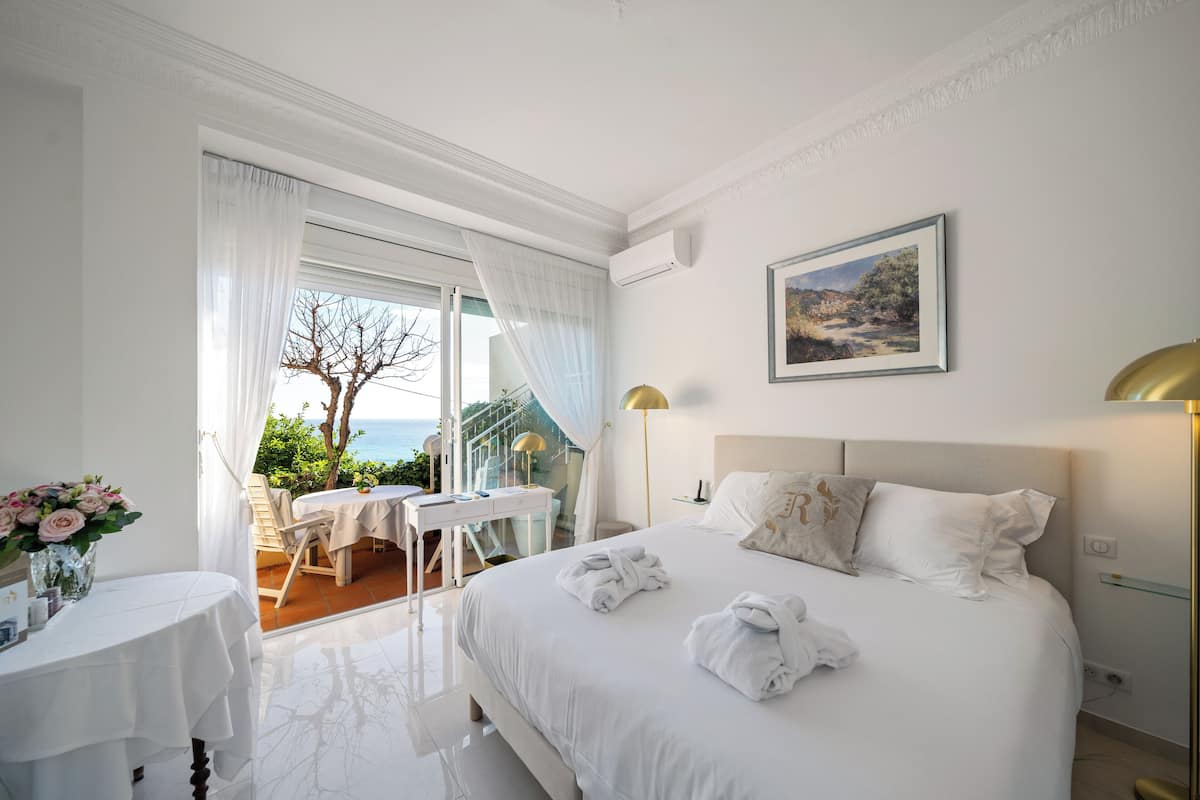 Ein Hotelzimmer mit einem großen Bett, einem Schreibtisch mit Stuhl, einem kleinen Tisch und Blick ins Freie.