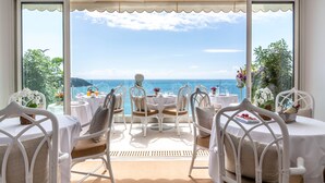 A terrace with white wicker furniture, round tables, and chairs, overlooking a scenic ocean view. - Le Roquebrune (Roquebrune-Cap-Martin)