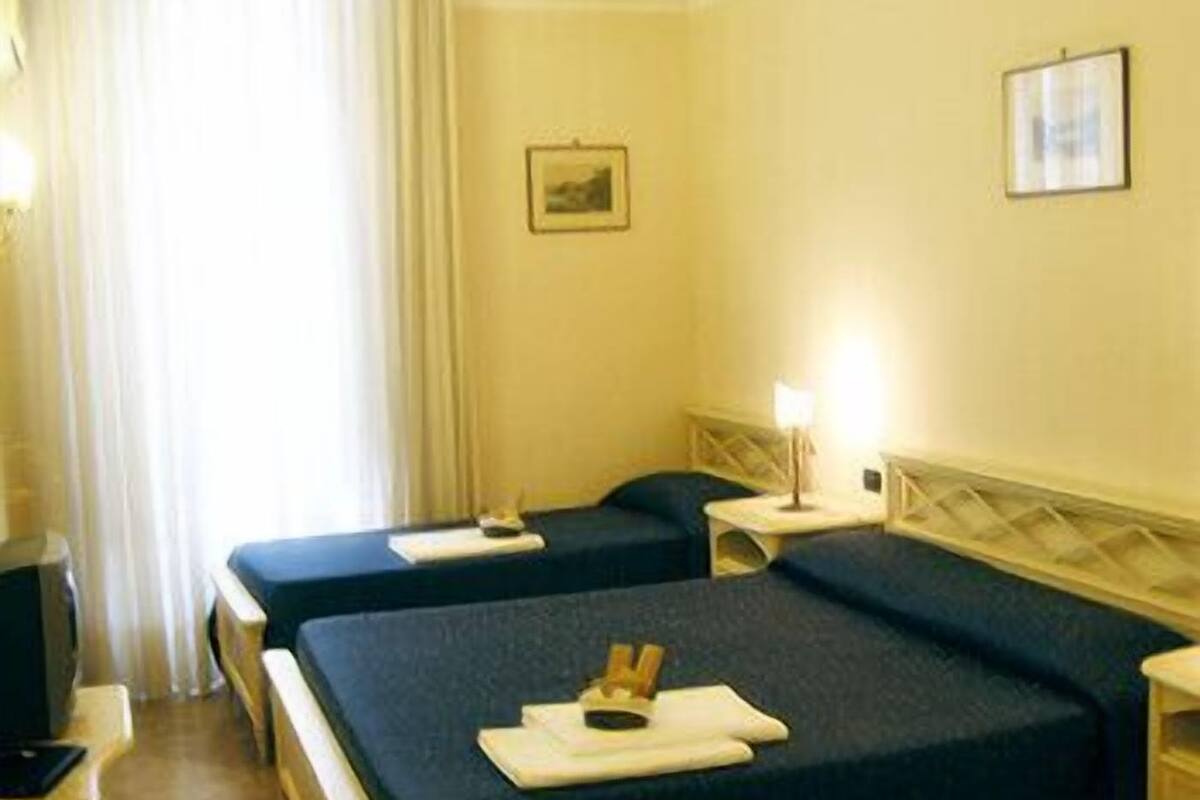 Ein Hotelzimmer mit zwei Betten, einem Schreibtisch, einem Stuhl und einem Fernseher.