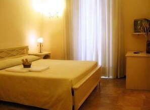 A hotel room with a bed, a nightstand with a lamp, a small table with a vase, and a window with curtains. - La Dimora di Nettuno (Naples)