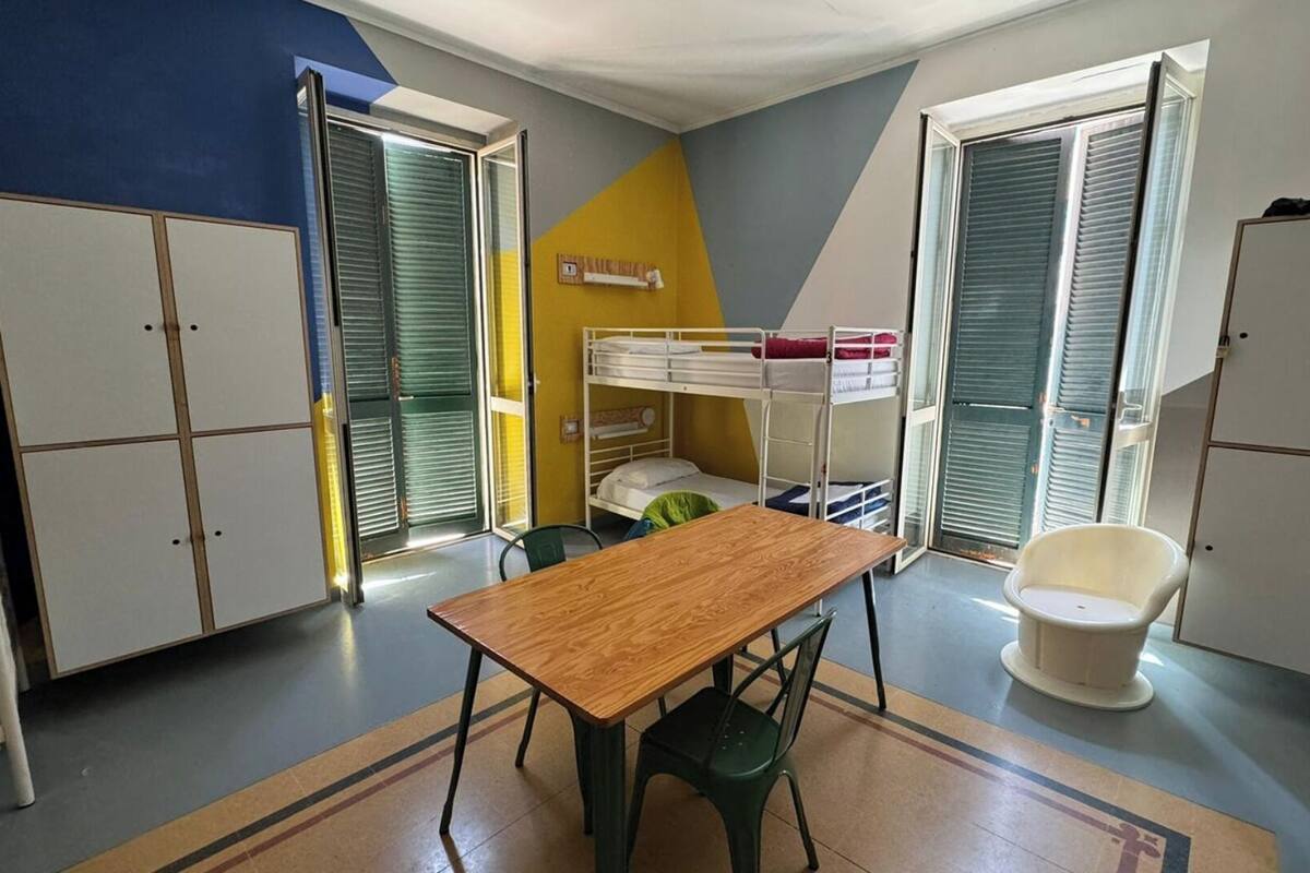 Une chambre de dortoir avec des lits superposés, une table en bois, une chaise verte et des armoires de rangement.