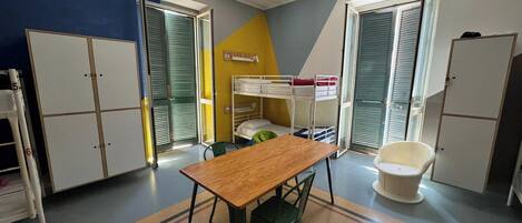 A dormitory room with bunk beds, a wooden table, a green chair, and storage cabinets.