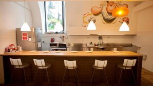 Een keuken met een centraal eiland, vier barstoelen, een koelkast, een magnetron en een raam.