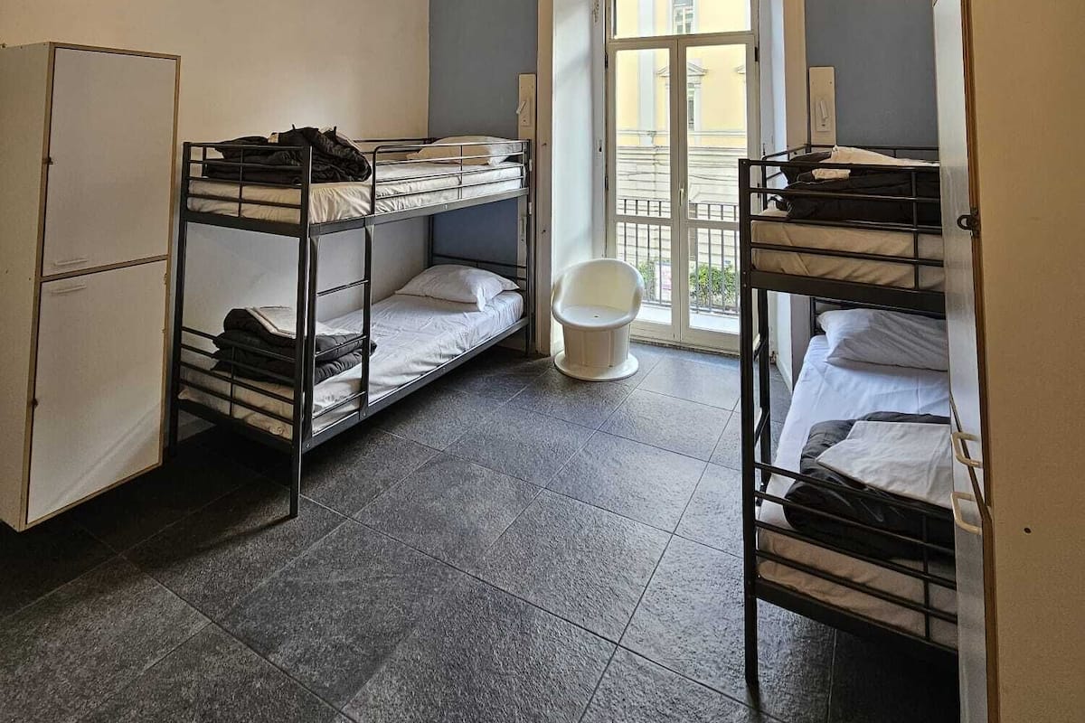 Une chambre de dortoir avec des lits superposés, des toilettes blanches et une porte donnant sur l’extérieur.