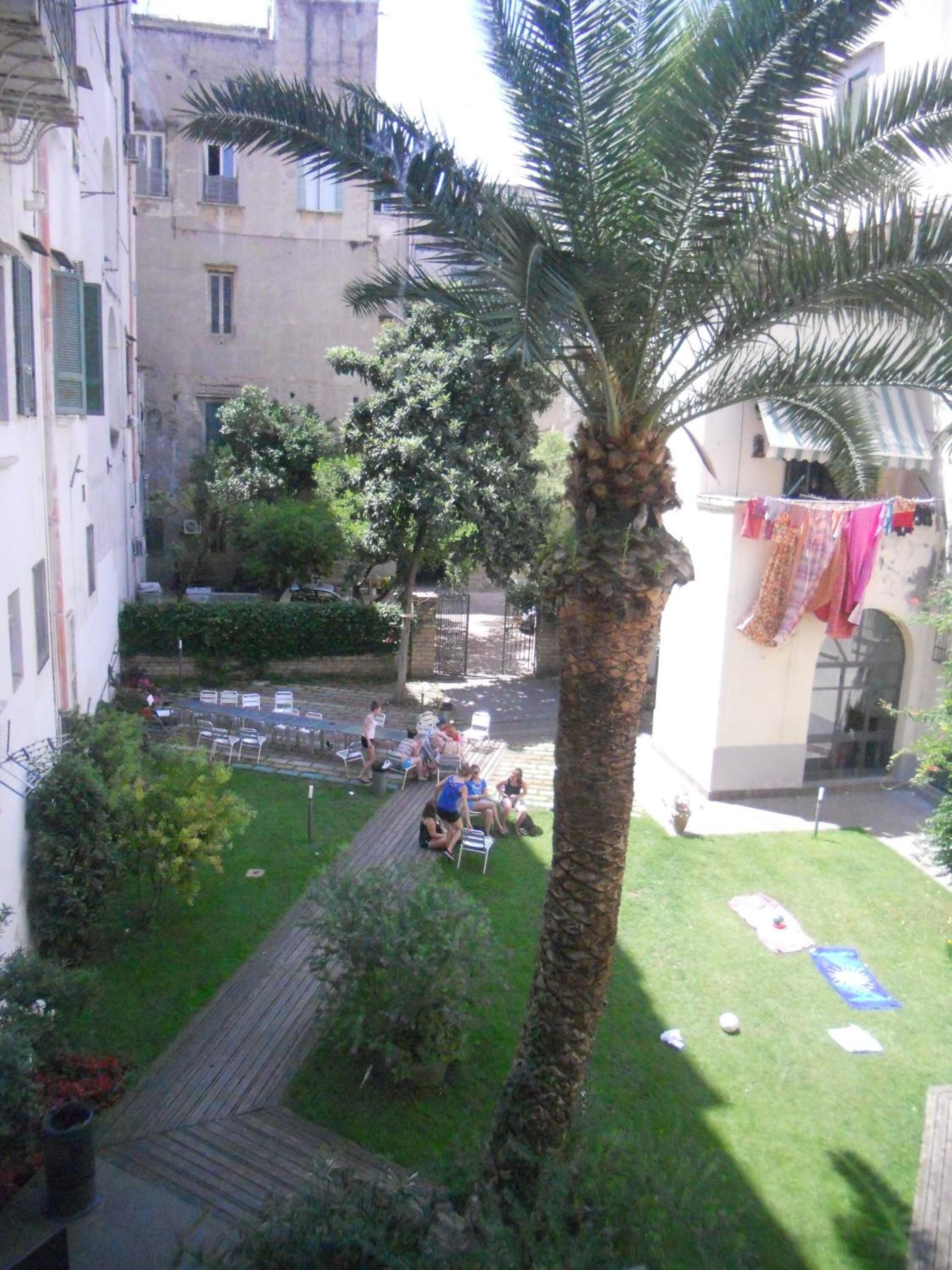 A courtyard with a palm tree, a seating area with people, and a building with laundry hanging.