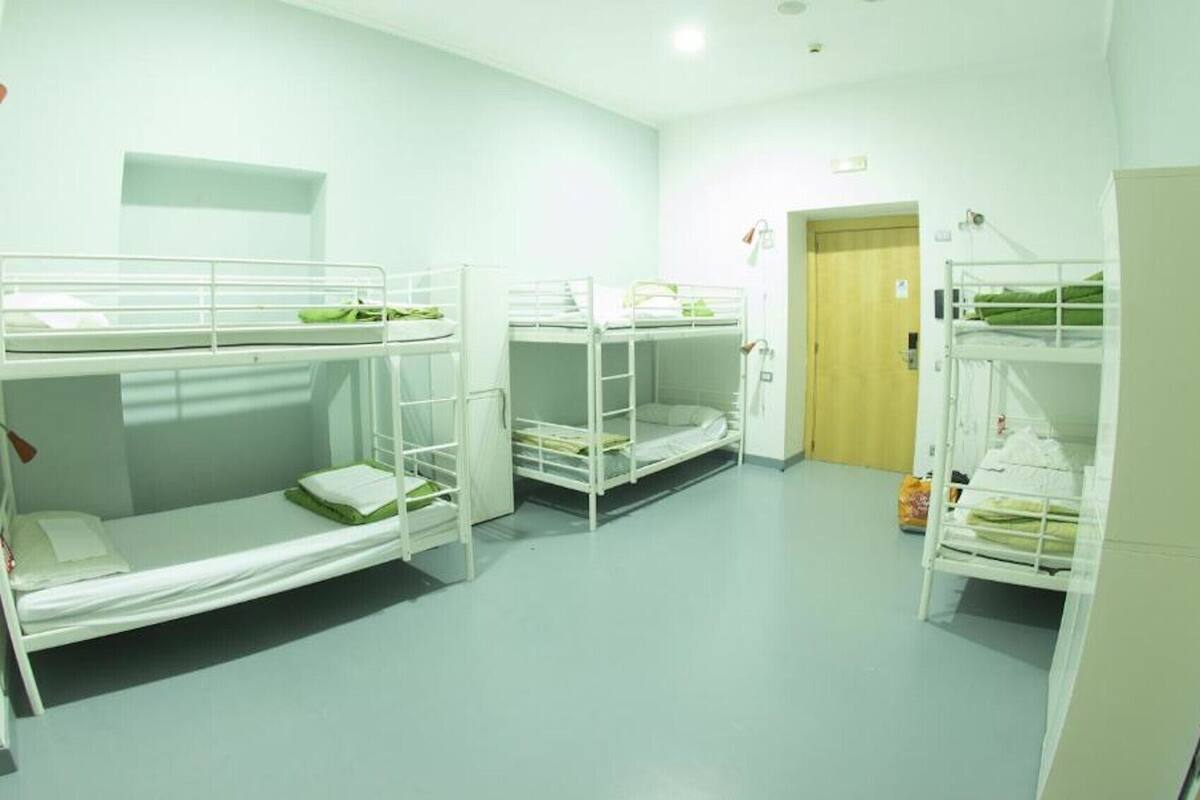 Une chambre de dortoir avec des lits superposés, une petite kitchenette et une porte donnant sur une autre pièce.