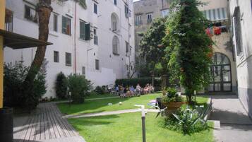Un patio con césped, una palmera y un grupo de personas sentadas en mesas.