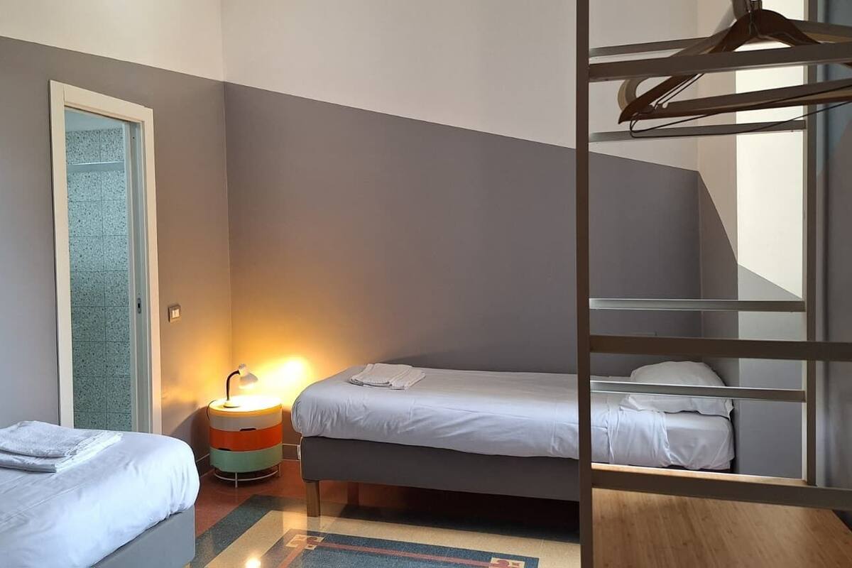 Une pièce avec deux lits, un fauteuil suspendu, une porte et une lampe.