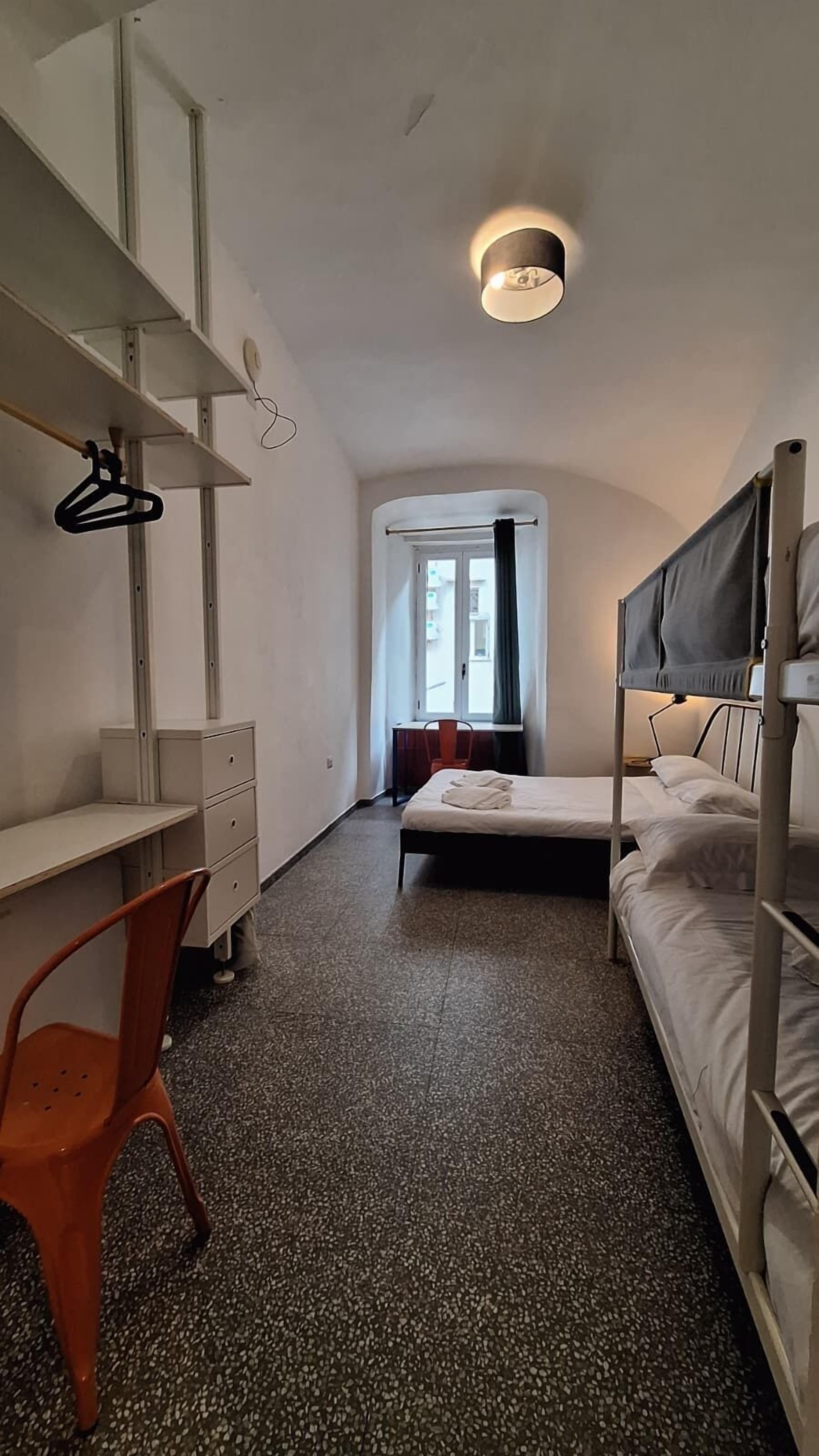 Quarto com beliches, uma escrivaninha, uma cadeira, um guarda-roupa e uma janela com cortinas.