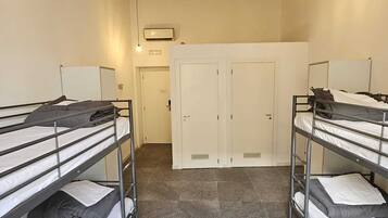A dormitory room with bunk beds, a white wardrobe, and a door in the background.