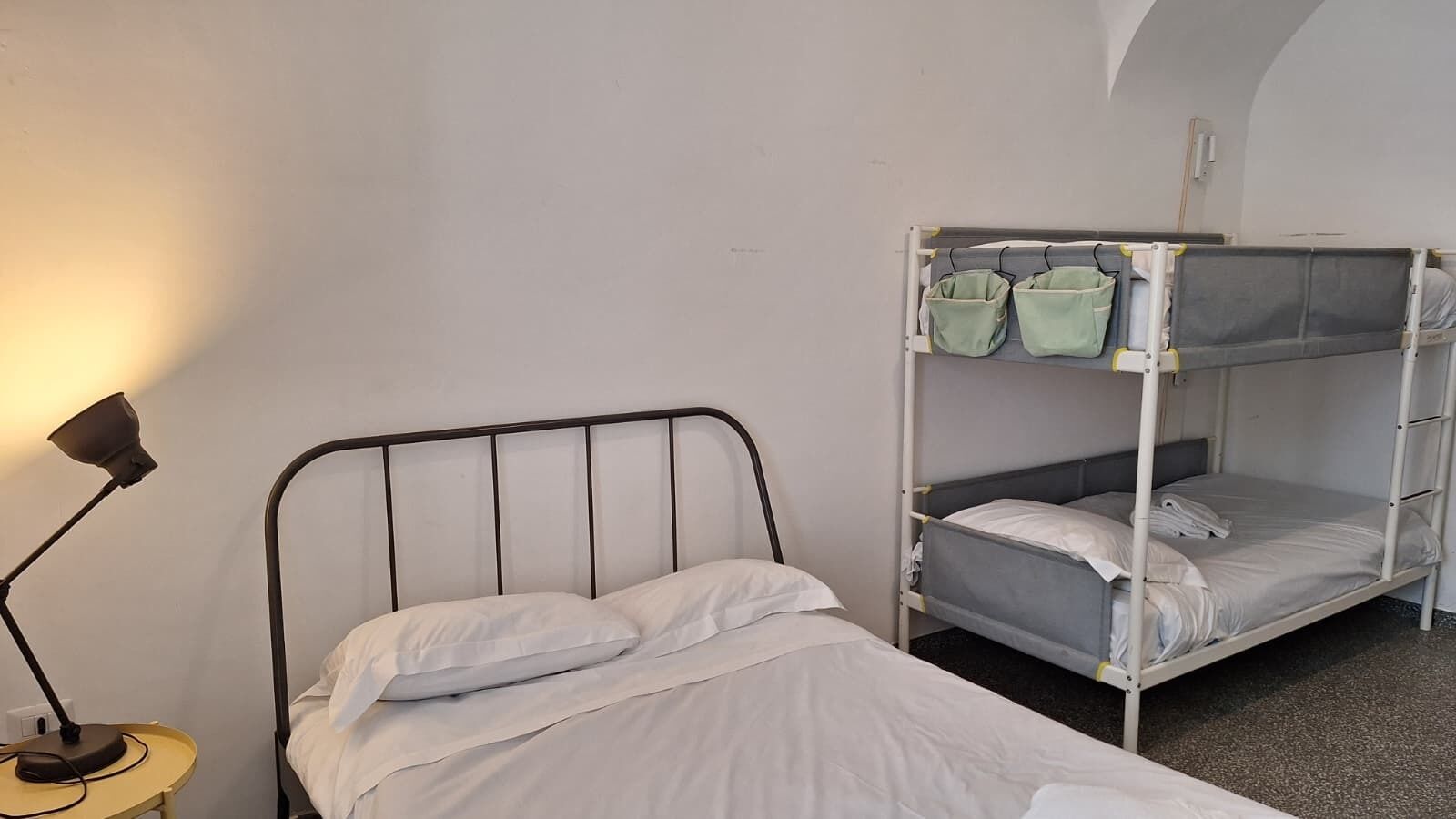 A single bed with a metal frame, a bedside lamp, and a bunk bed with two levels.