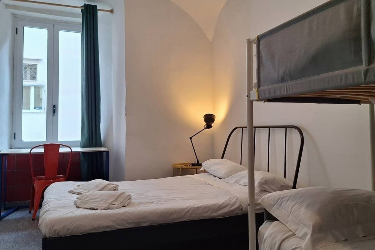 Une chambre avec un lit superposé, un bureau avec une chaise, une lampe et une fenêtre avec des rideaux.