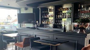 A bar area with a counter, stools, and a television. - Hôtel Saint Jean (Wimereux)