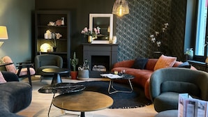 A modern living room with a sofa, armchairs, a coffee table, a fireplace, and decorative items. - Hôtel Saint Jean (Wimereux)
