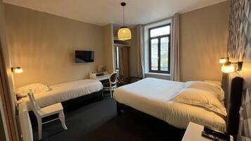 Une chambre d’hôtel avec deux lits simples, un bureau, une chaise, une télévision et une fenêtre avec des rideaux.