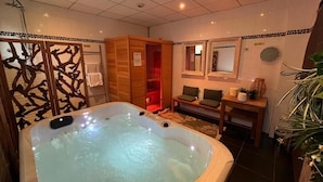 A spa room with a hot tub, wooden cabinets, a mirror, and a small table with a plant. - Hôtel Saint Jean (Wimereux)