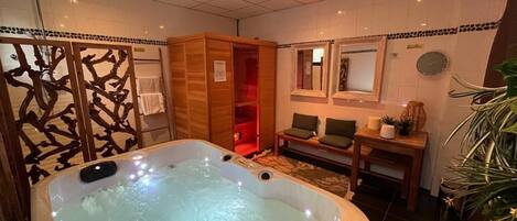 A spa room with a hot tub, wooden cabinets, a mirror, and a small table with a plant.