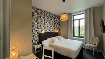 A hotel room with a bed, bedside tables, a chair, a desk, a lamp, and a window with a view.