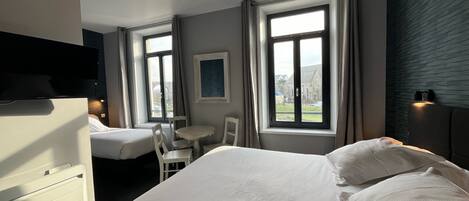 A hotel room with a large bed, a desk, two chairs, a TV, and a window with curtains.