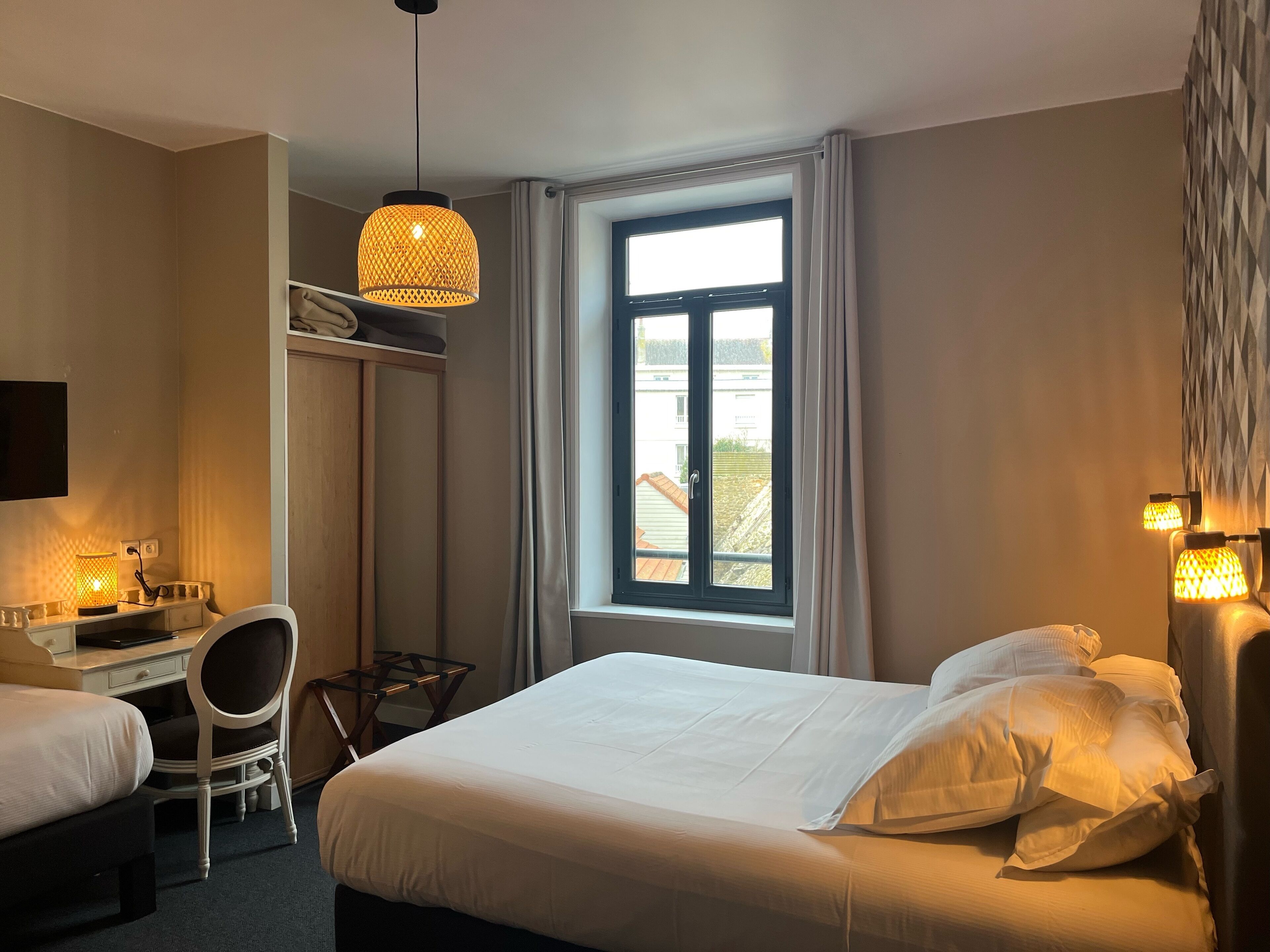 Una habitación de hotel con cama, escritorio, silla y ventana con cortinas.