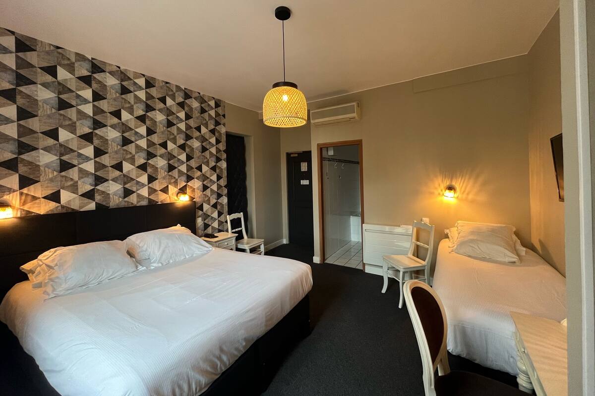 A hotel room with two beds, a geometric patterned wall, a hanging light fixture, and a door leading to a bathroom.