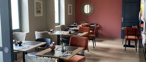 Un espace repas avec plusieurs tables et chaises, un grand miroir rond accroché au mur et une porte sur le côté droit.