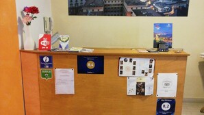 A hotel reception desk with a cityscape view, various awards, and a vase with flowers. - B&B Rainbow (Naples)