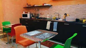 A small kitchen with a microwave, sink, and various kitchen items. There are colorful chairs and a table with a patterned tablecloth. - B&B Rainbow (Naples)