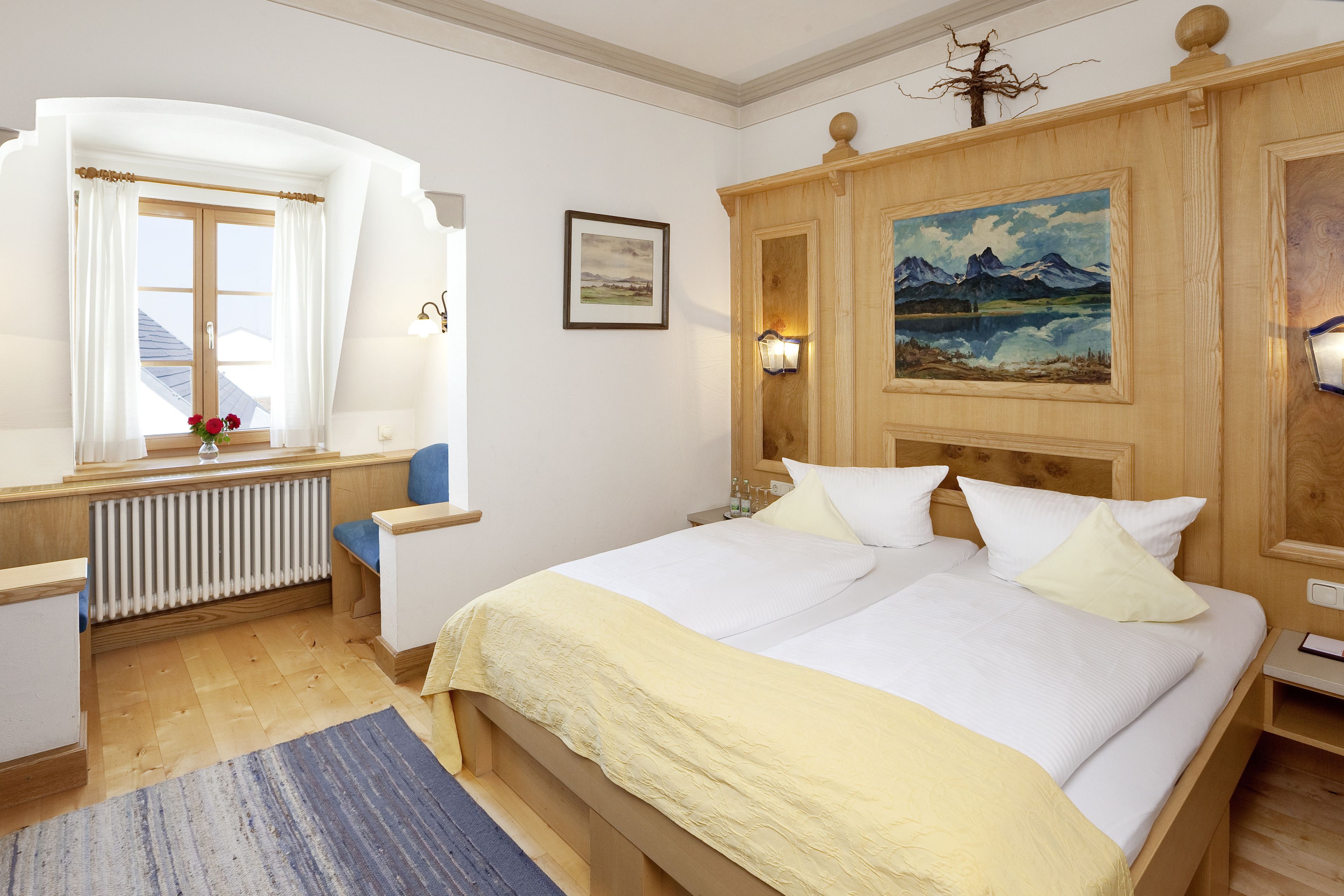 Quarto com cama de madeira, janela com cortinas, radiador e um quadro na parede.